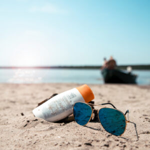 Sun lotion and sunglasses on the sea sand beach. Summer Holiday cream protection on sunny day. Copy space